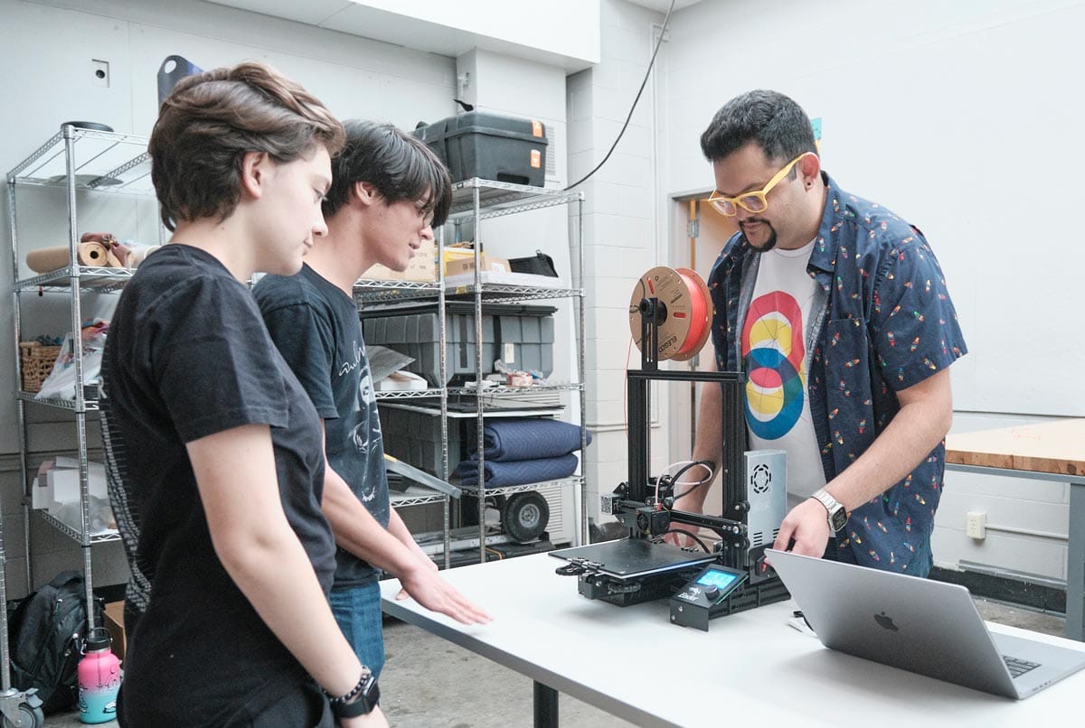 Juan Carlos Noguera standing in a studio demonstrating to two of his students.