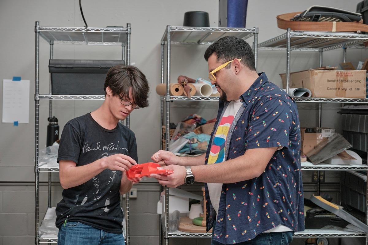 Juan Carlos Noguera standing in a studio working on a design with a student.