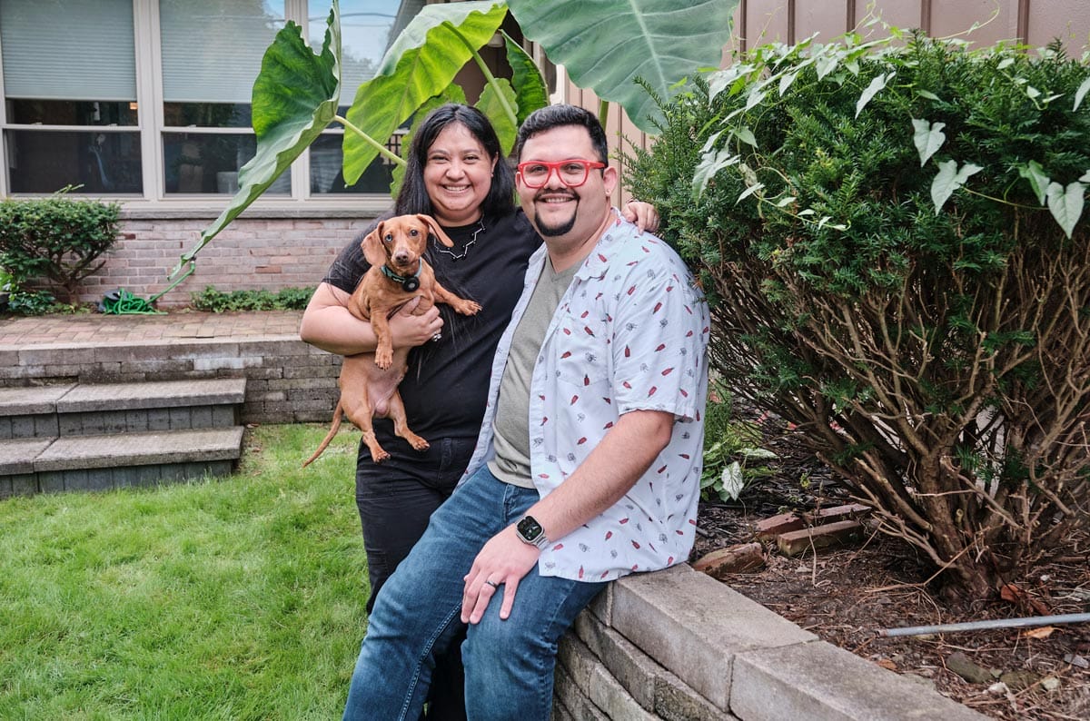 Juan Carlos Noguera in his backyard smiling with his family member and pet dachshund.