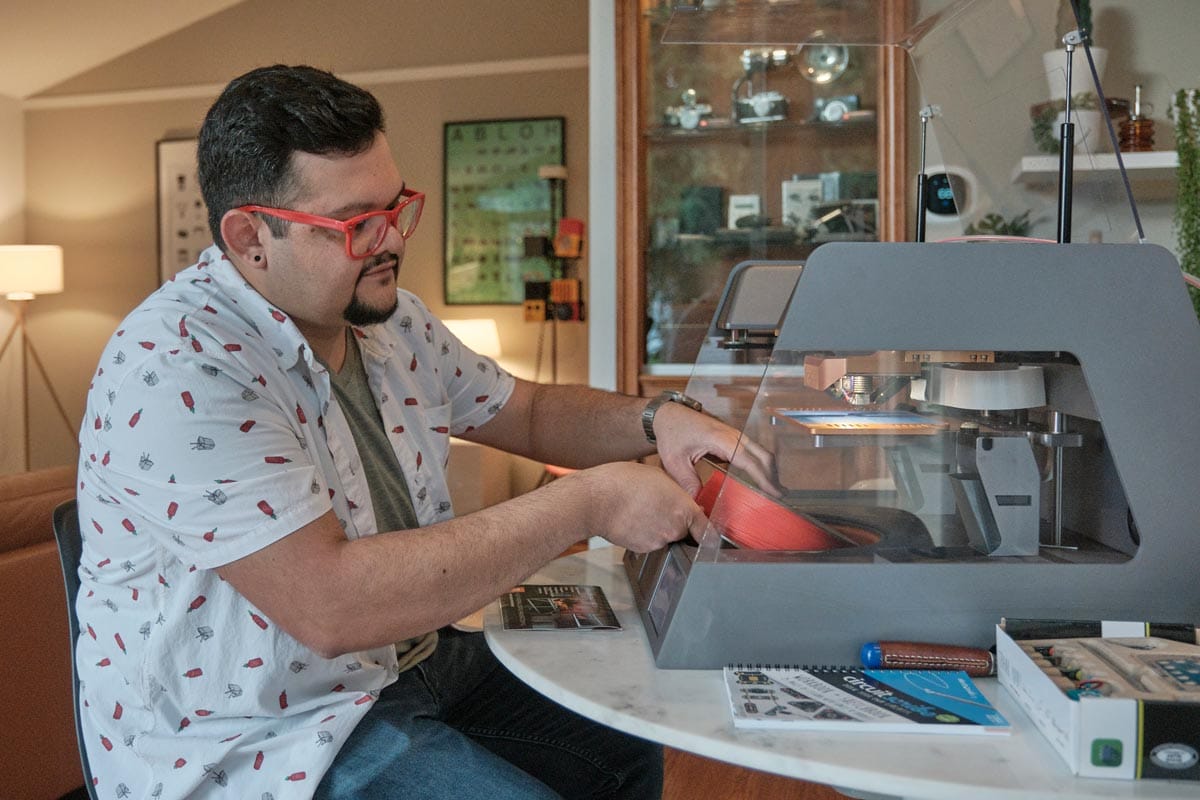 Juan Carlos Noguera sitting in front of a small 3D printer.