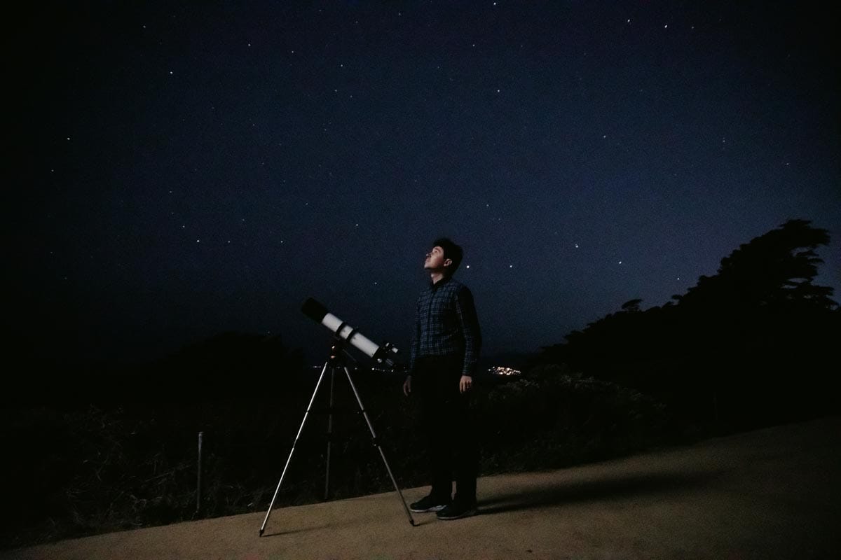 Tomasz Nowakowski stands next to a telescope pointed towards the stars.