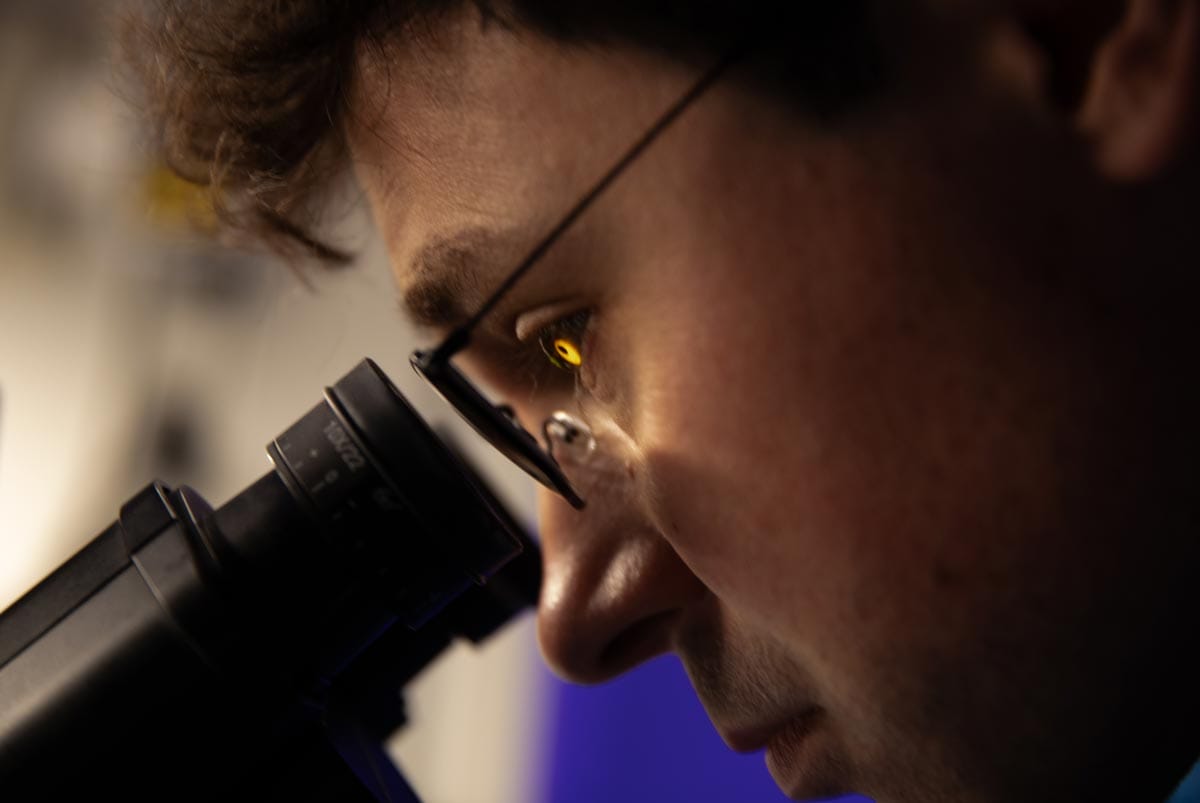 A close up of Tomasz Nowakowski as he looks into a microscope.