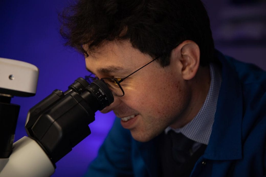 A close-up of Tomasz Nowakowski's face as he peers into a microscope.
