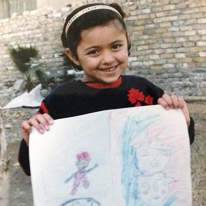 A photo of Maryam Turkey as a child holding up drawings she made.