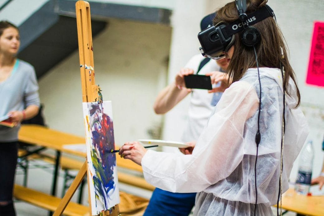 A woman painting on a canvas while wearing a VR headset.