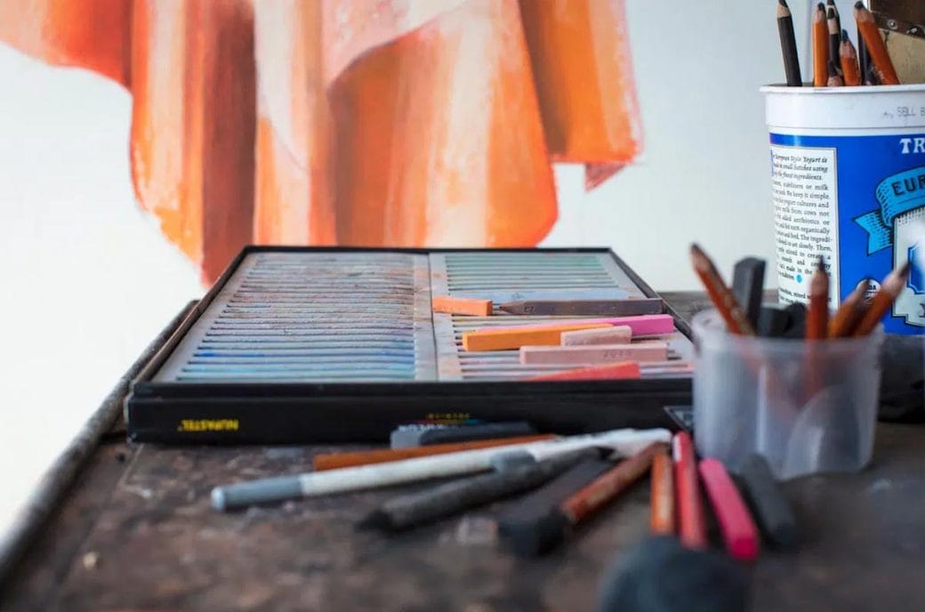 A box of pastels on a table with other artistic tools.