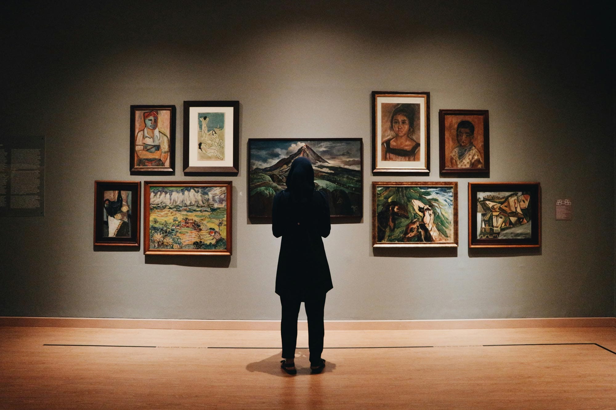 A person standing in front of a gallery wall with art works hung on it.
