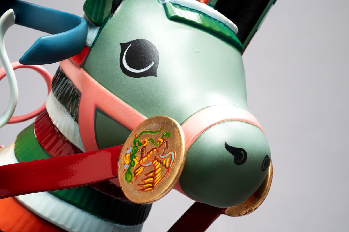 A detail shot of the green face of a multicolor piñata-inspired donkey sculpture with a detailed gold rein.