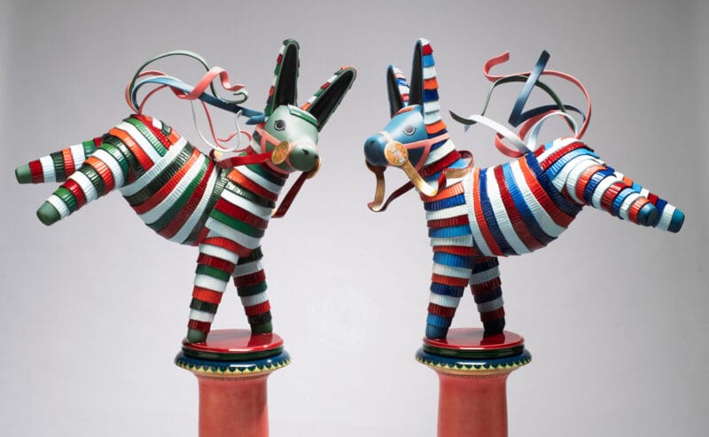 A medium shot of two multicolor piñata-inspired donkey sculptures: one is red, green and white, and the other is red, white and blue.