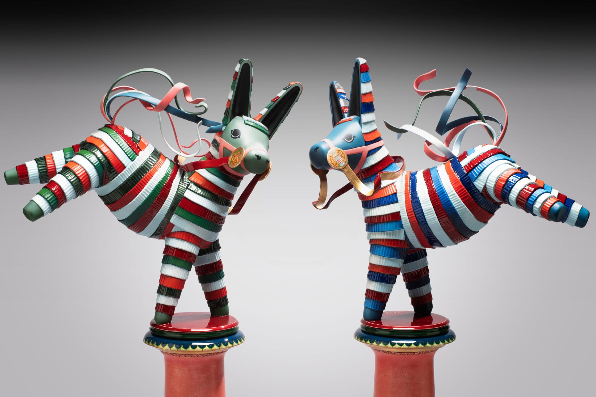 A medium shot of two multicolor piñata-inspired donkey sculptures: one is red, green and white, and the other is red, white and blue.