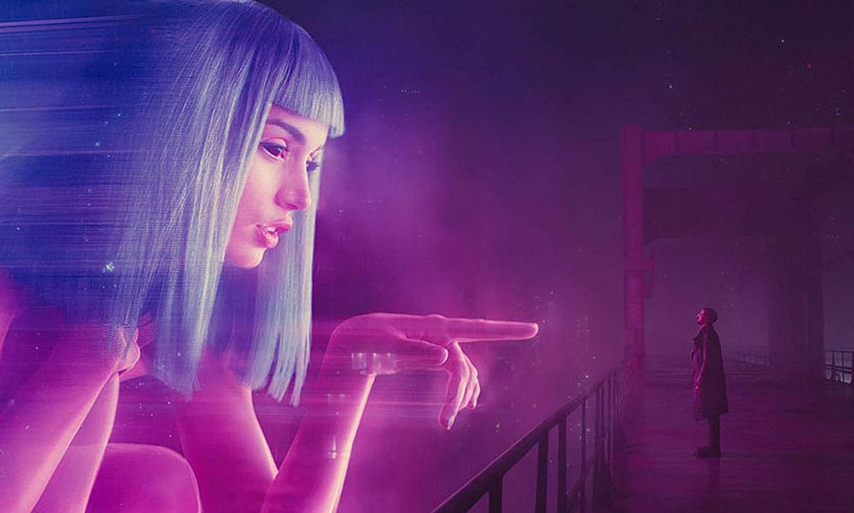 A large digital virtual figure crouches and points at actor Ryan Gosling’s character, K, in the 2017 film, Blade Runner 2049.