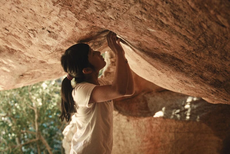 Ashima touches crevices in a rock overhang, studying the surface for places to grip while attempting a climb.