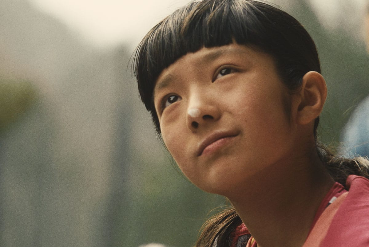 Japanese American rock climber Ashima Shiraishi as she gazes up at a climb with a pensive and bemused expression on her face. She has a smudge of white chalk on her nose.