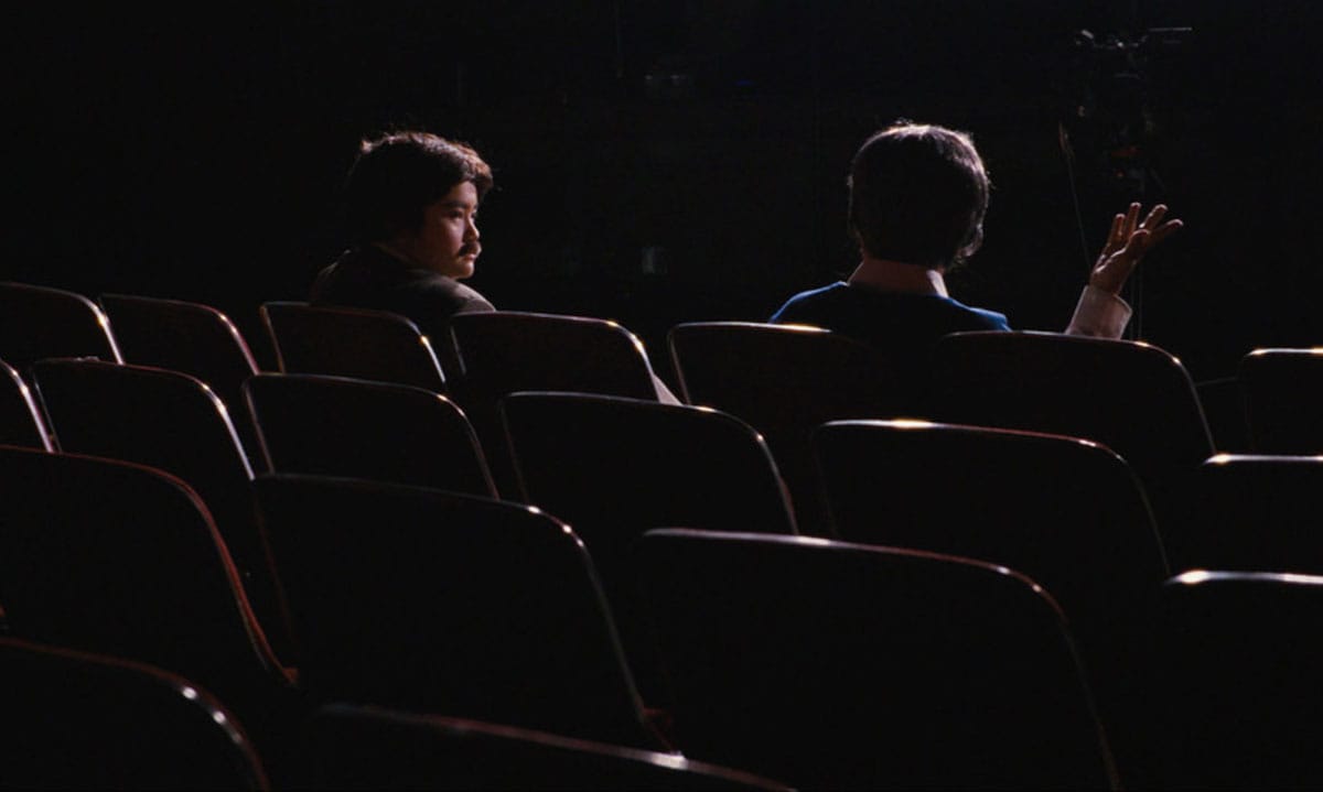 The film’s two female protagonists seated in a dark movie theater. They are dressed as men.