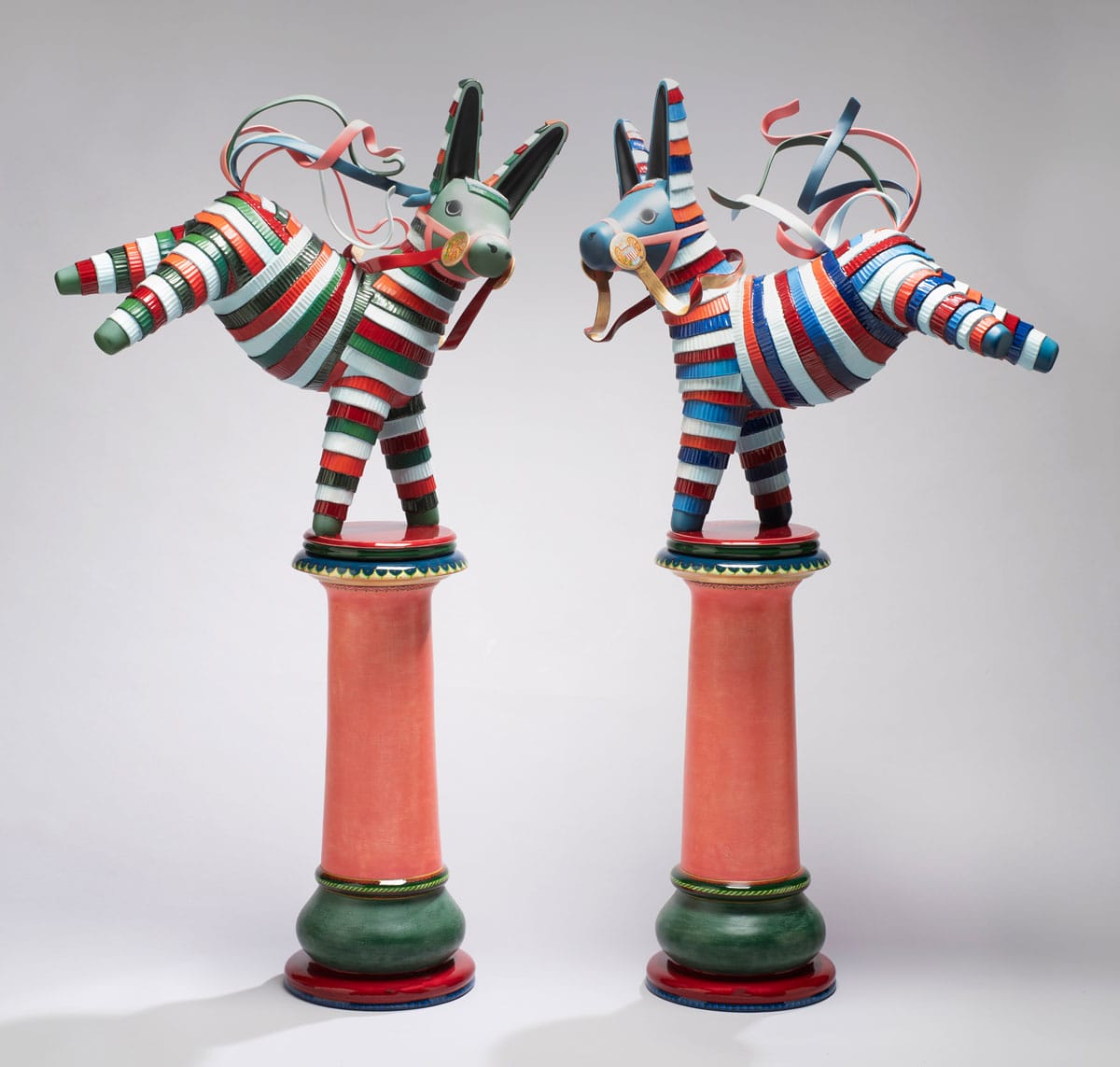 Two multicolor piñata-inspired donkey sculptures standing on pedestals.