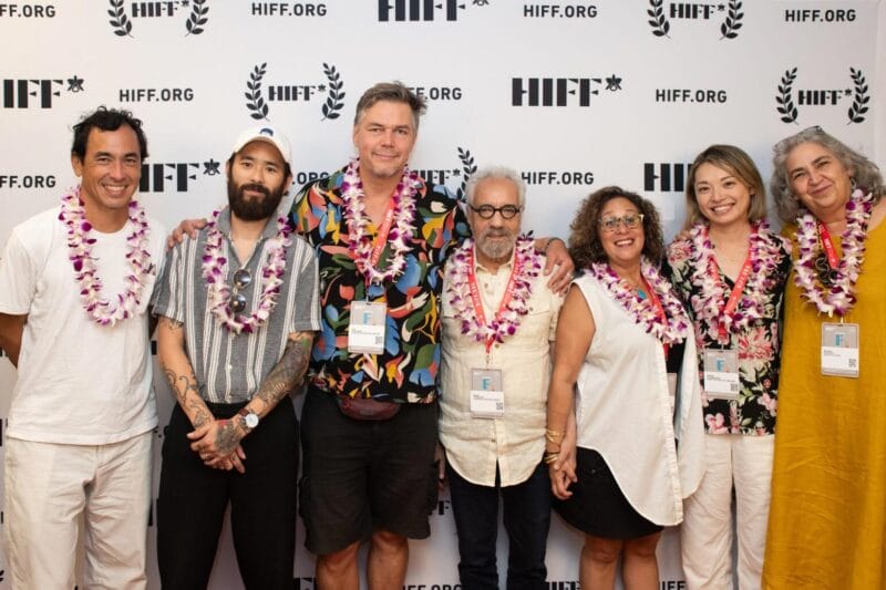 Filmmakers in leis standing on front of a HIFF step and repeat.