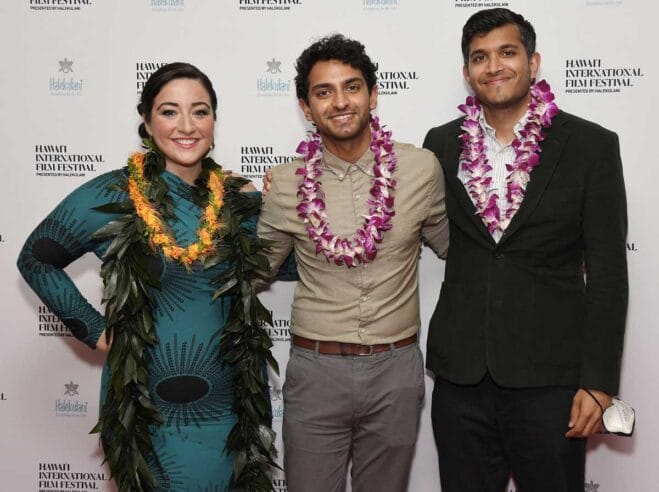 Karan Soni and Roshan Sethi in front of the step and repeat wearing leis.