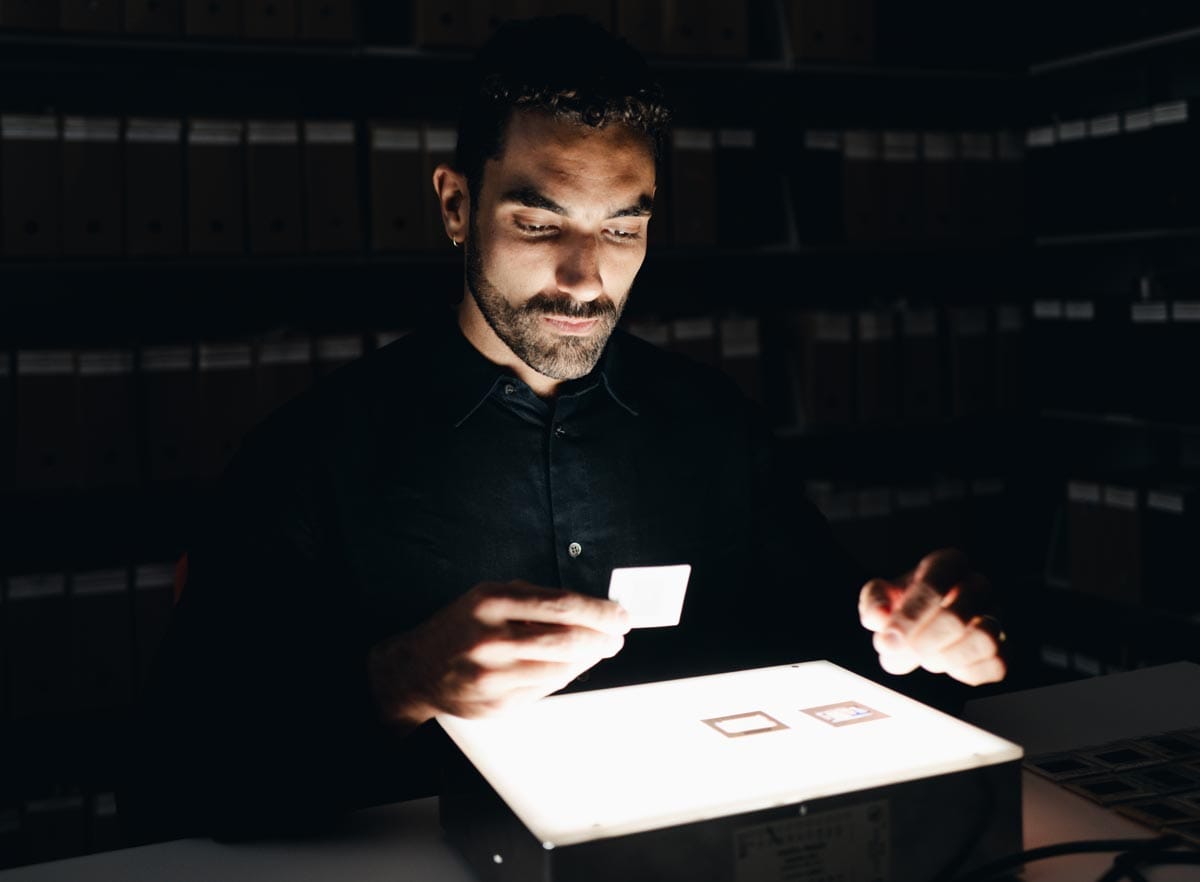 Bernardo in a dark room studying a film negative on top of a light box.