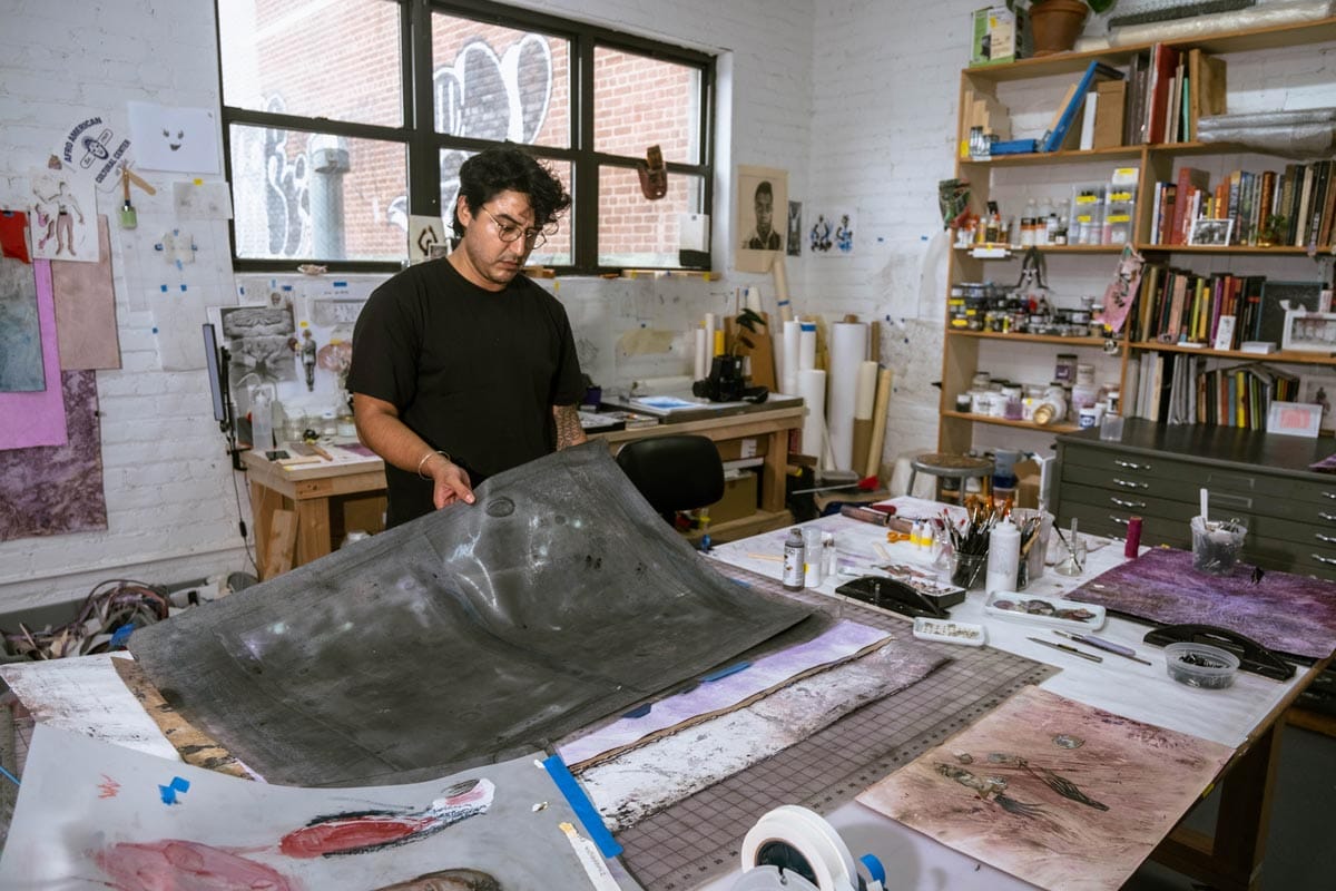 Felipe standing at a desk in his studio and working with fabric.