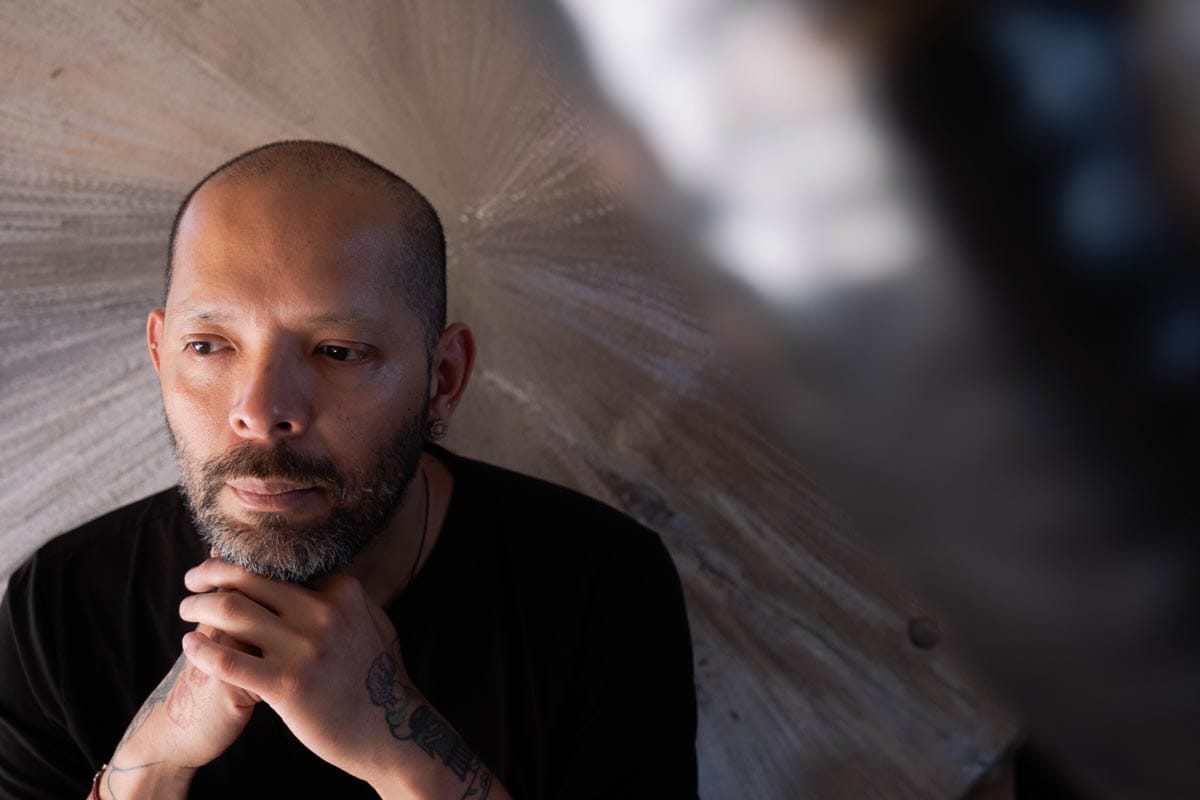 Guadalupe rests his head on his hands as he sits in front of one of his large metal artworks.