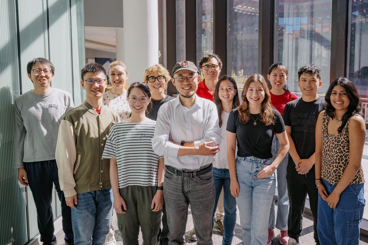 Guosong stands smiling with eleven of his lab members.