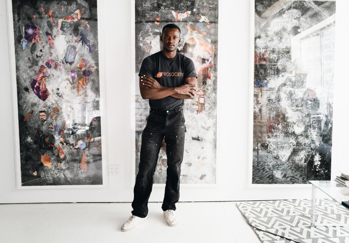 Jeffrey standing with his arms folded in front of three large collaged works.