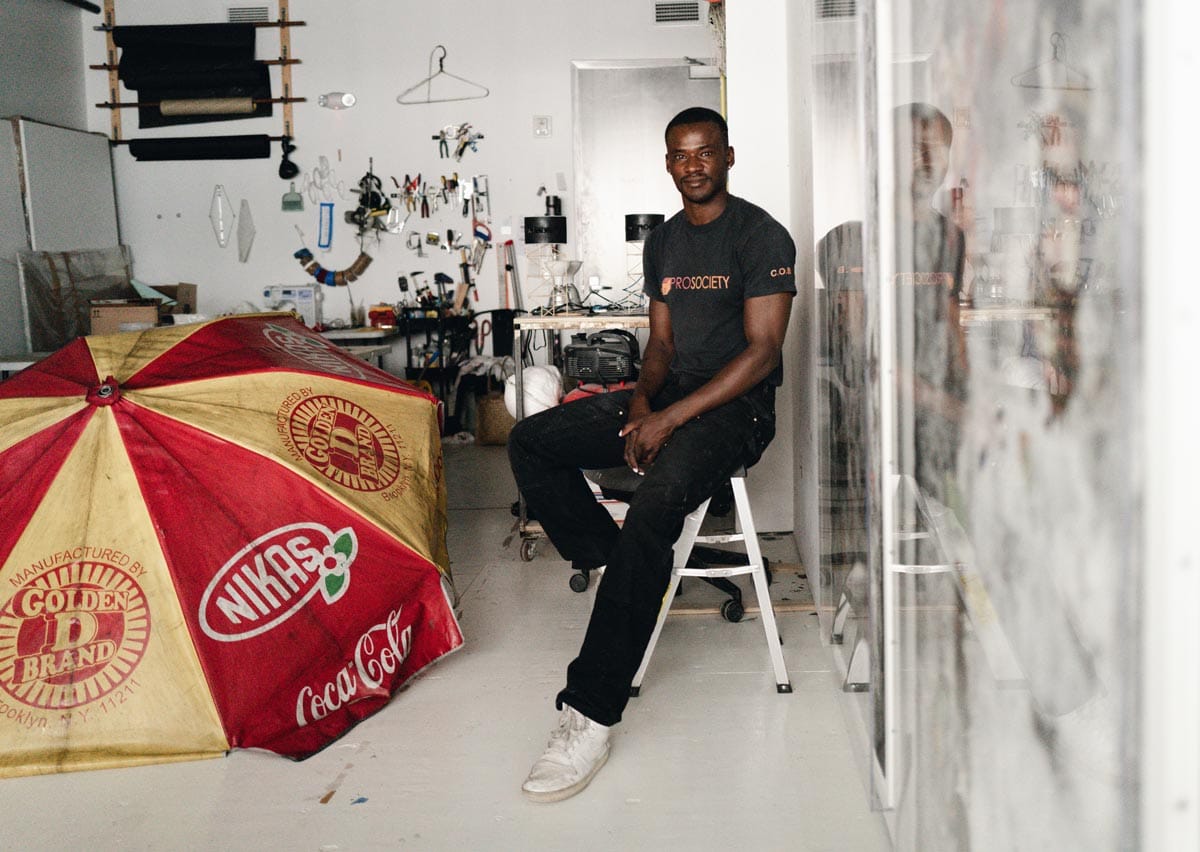 Jeffrey sitting on a step-ladder in his studio next to a found object intended for his artwork: a red and yellow umbrella.