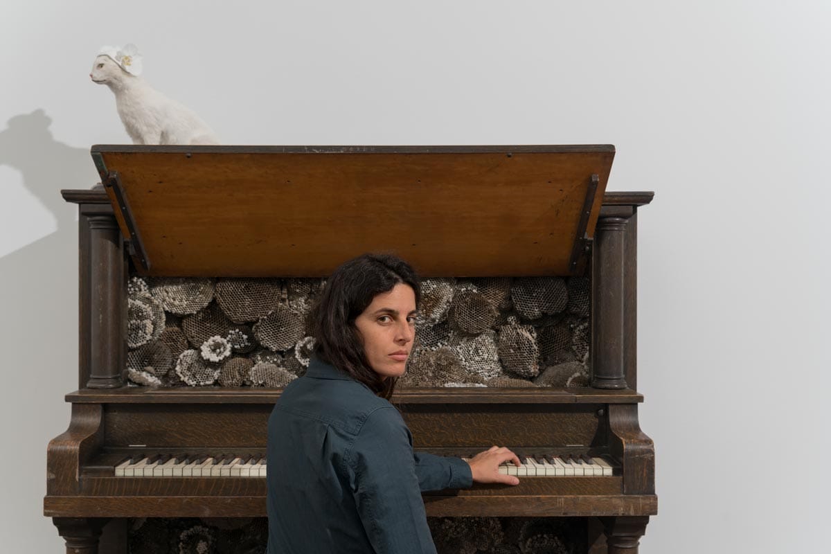 Selva sitting in front of one of her artworks: a piano with a taxidermy cat on top of it.