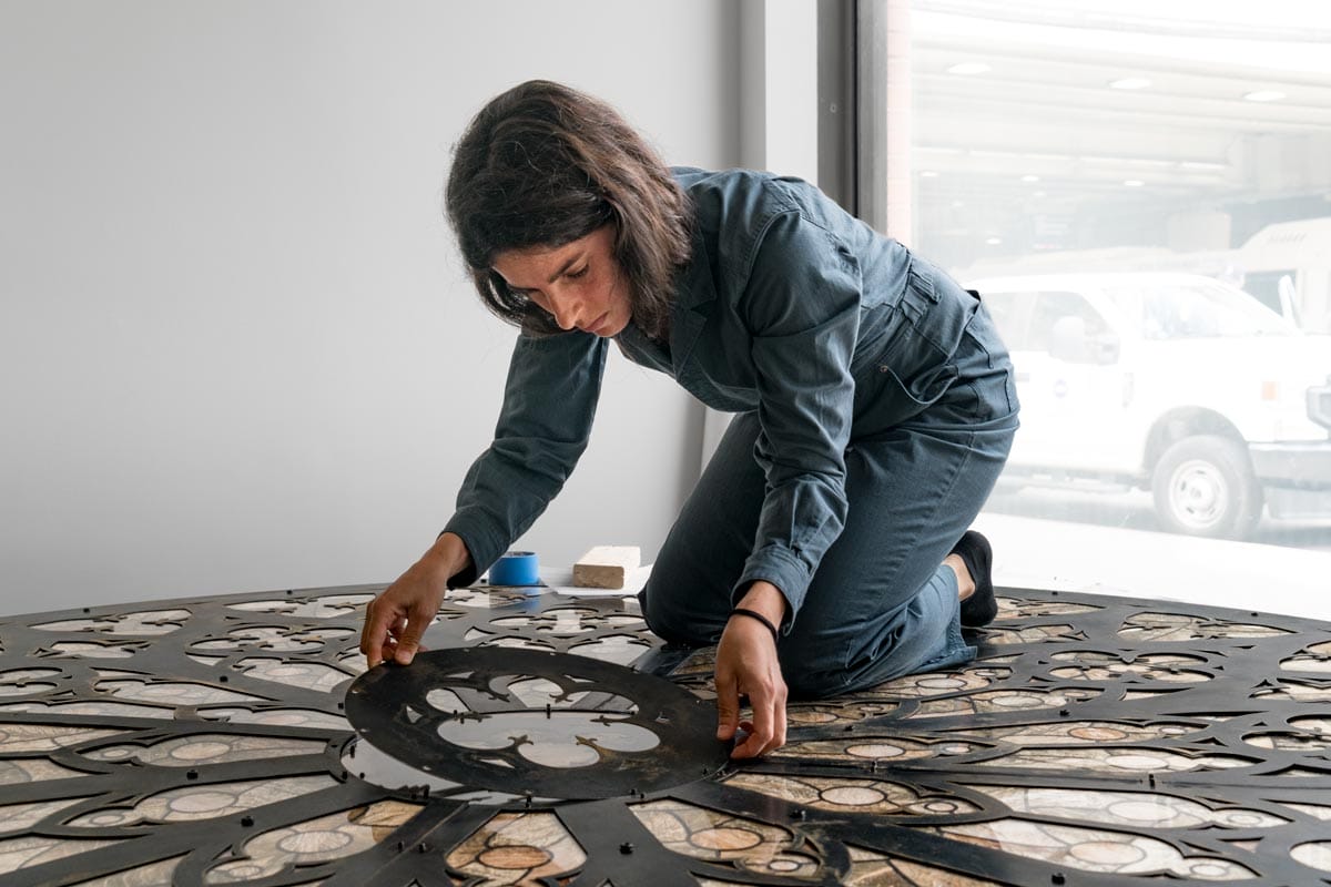 Selva kneeling on a large artwork as she places an ornate piece in the middle.