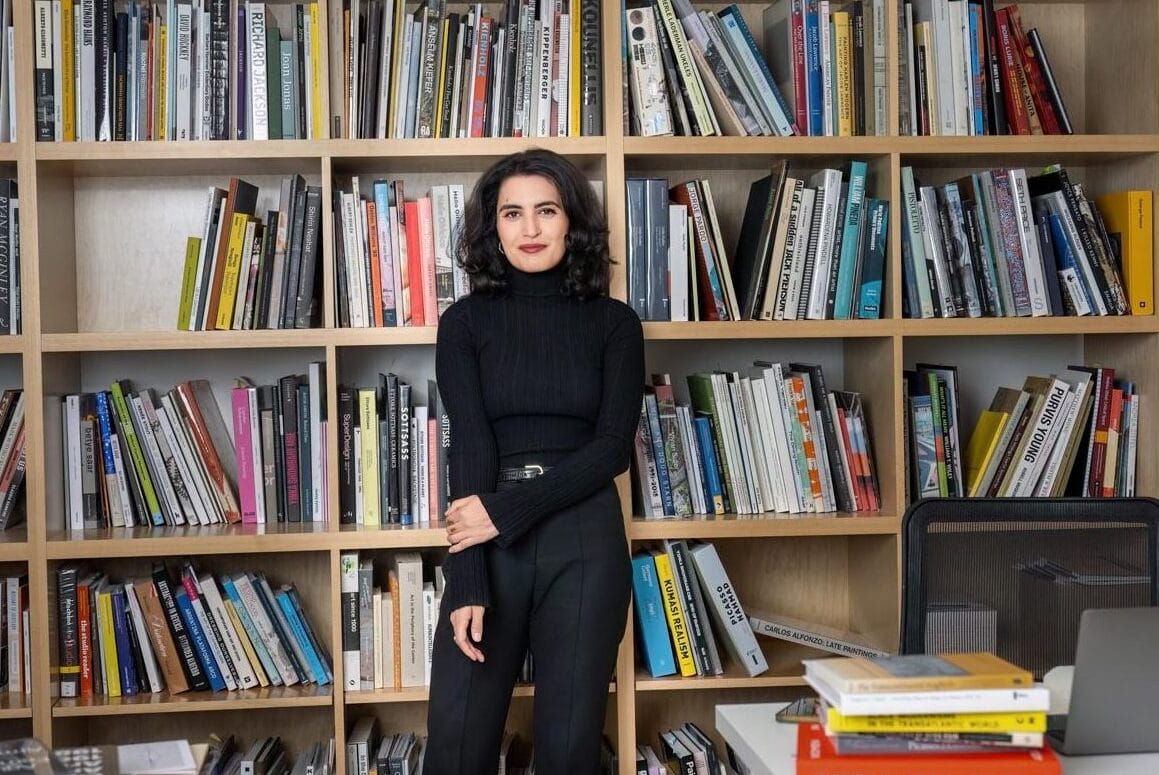 Donna standing in front of a large wooden bookcase filled with colorful books.