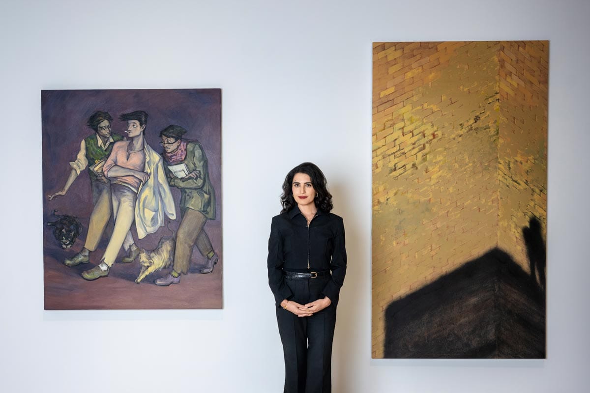 Donna standing in a gallery in the middle of two paintings by Li Ran (left) and Mohammed Sami (right.