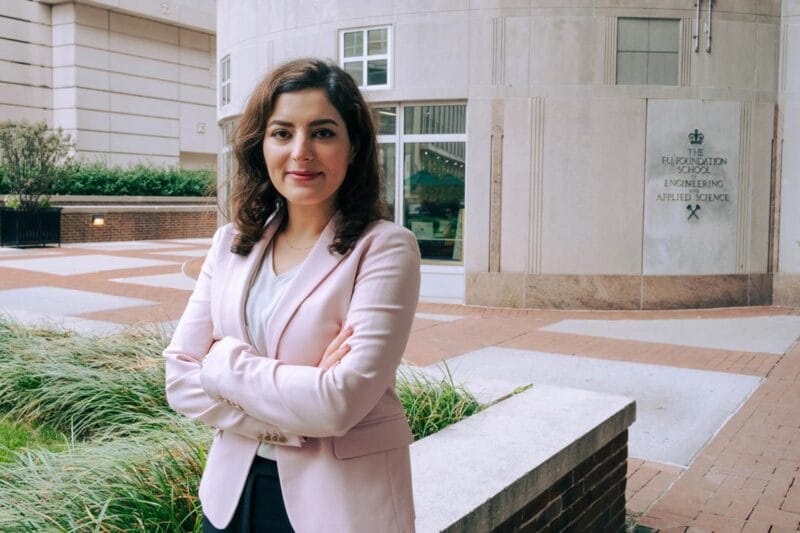 A portrait of Elham in a pink blazer in front of the Columbia University engineering building.