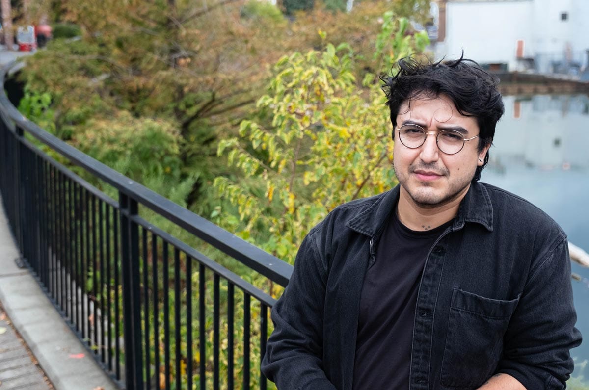 Felipe Baeza leaning on a barrier with water a foliage visible behind him.