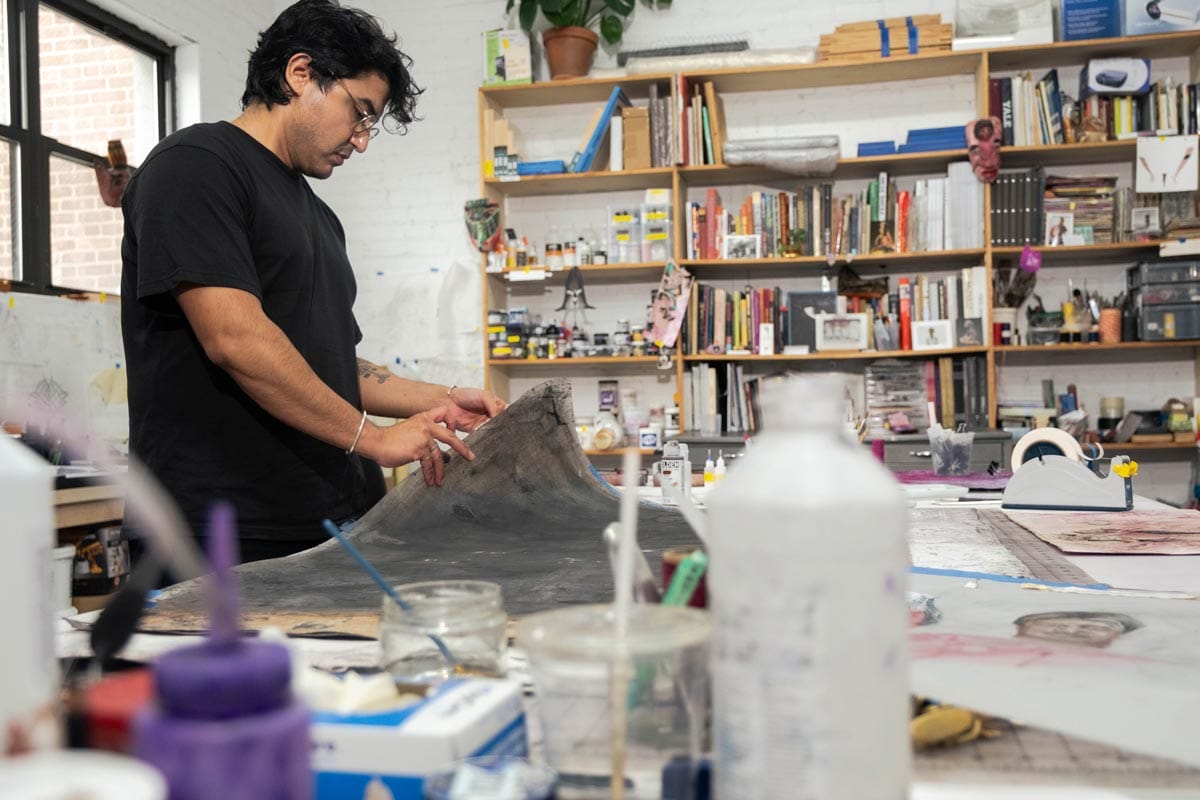 Felipe standing at the desk in his studio working with a gray, plastic sheet.