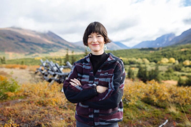 Francesca standing outside in nature in Alaska, smiling with her arms crossed.