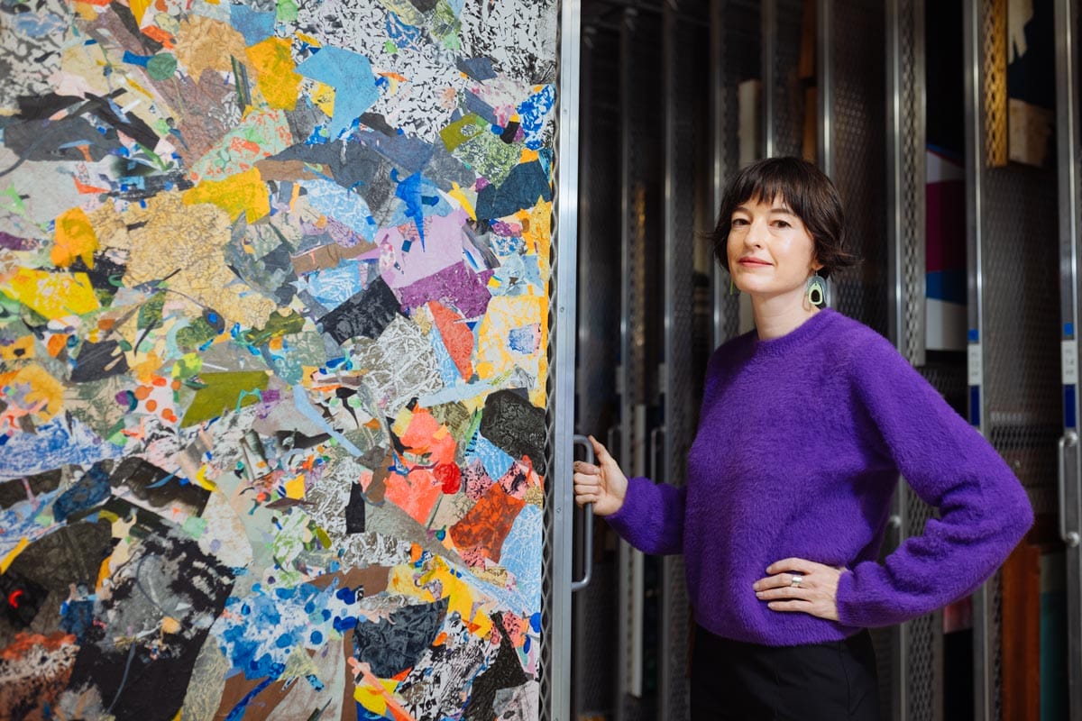 Francesca standing in art storage next to a large abstract painting on a storage rack.