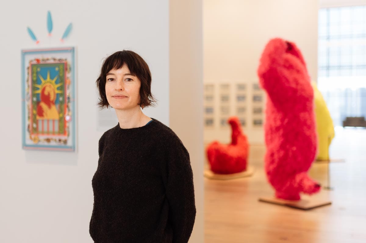 Francesca standing in a gallery with large red sculptures visible behind her.