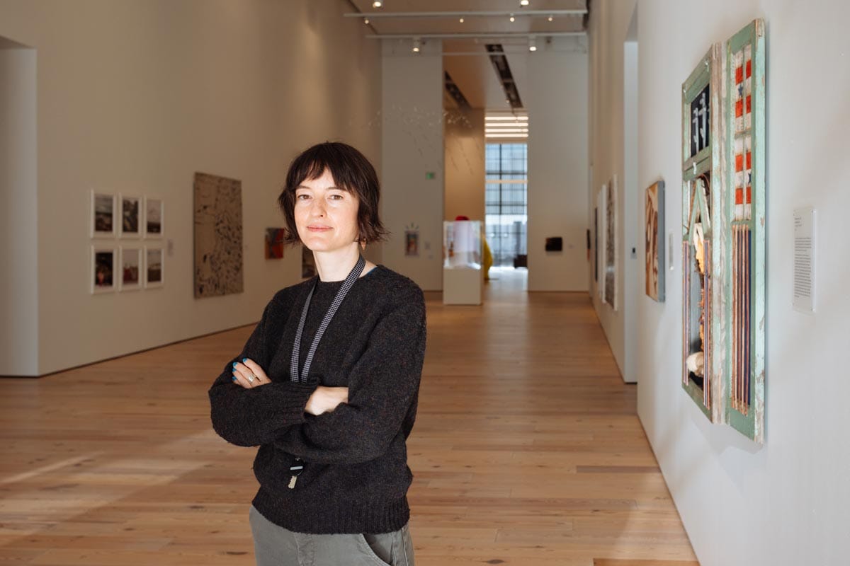 Francesca standing in a gallery space with canvases hanging on either side of the room.