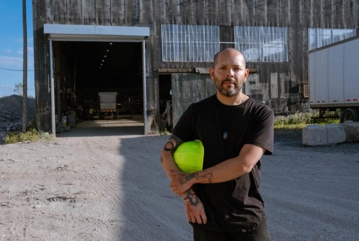 Guadalupe stands on a construction site with a neon yellow helmet tucked under his arm.