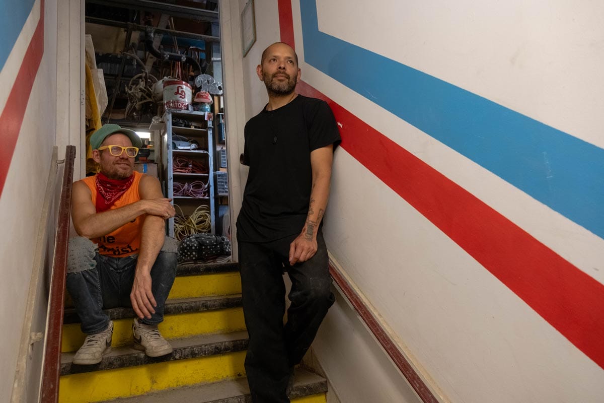 Guadalupe (right) and Billy Duffle (left) posed on the stairs of a work room/studio.