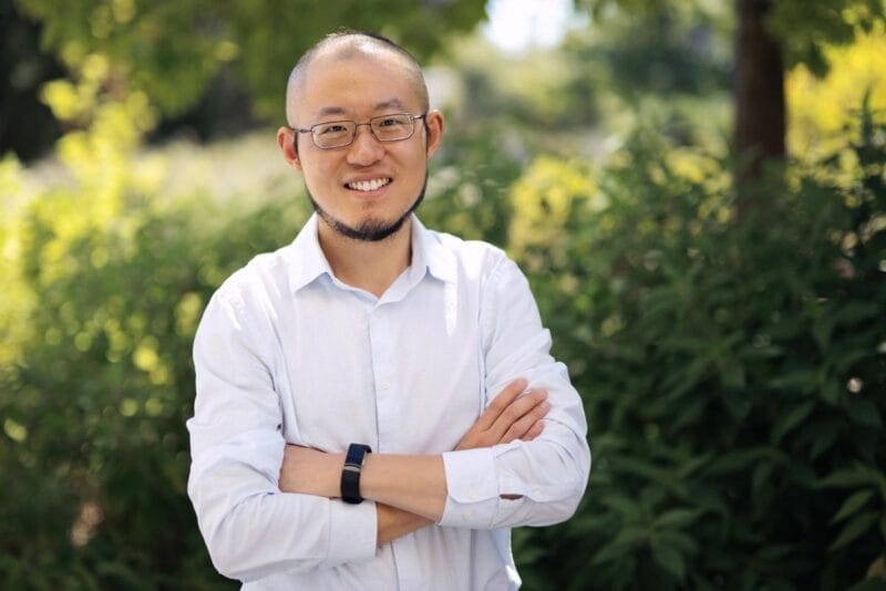 Guosong Hong standing in a garden and smiling with his arms folded.