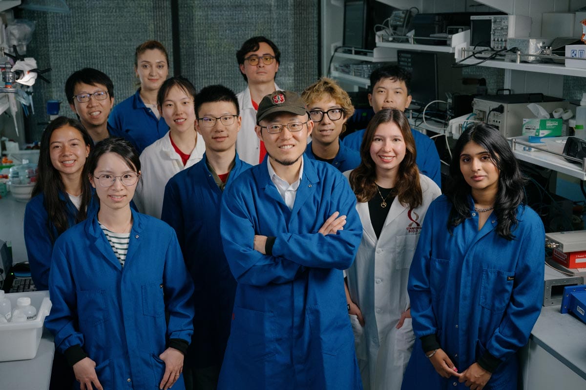 Guosong and eleven of his lab members - all wearing blue or white lab coats.