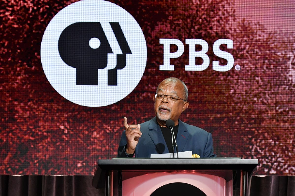 Henry Louis Gates Jr. standing at a podium with the PBS logo behind him.