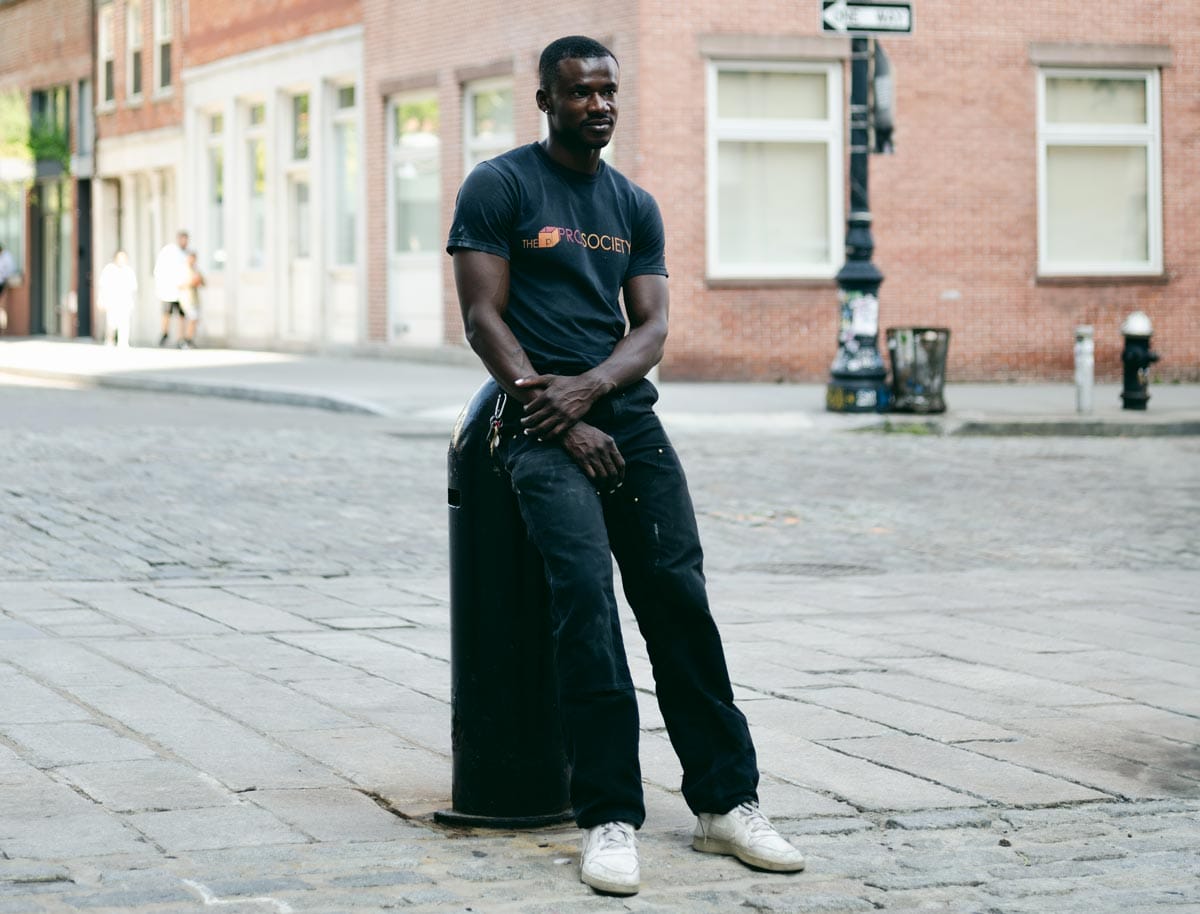 Jeffrey leans against a large stanchion on a cobble-stone street in the Financial District.