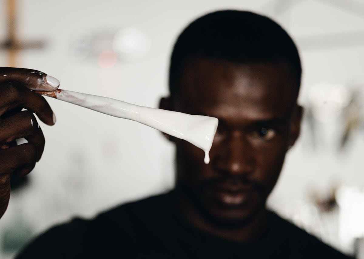 Jeffrey holds a paintbrush with white plaster on it in front of his face.