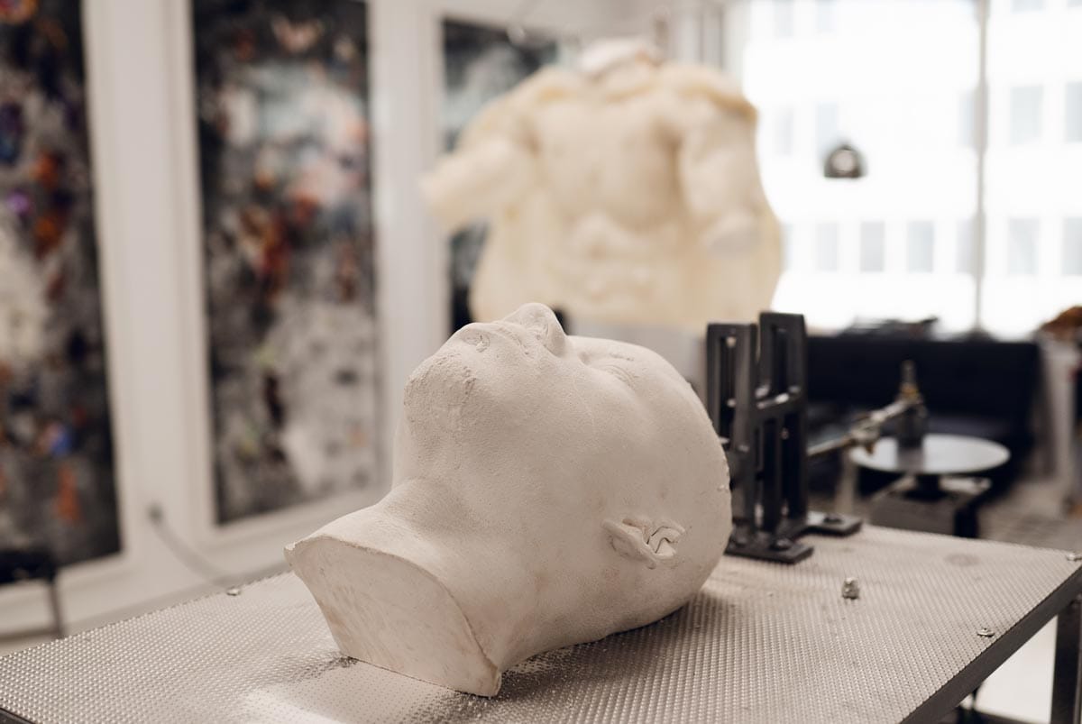 Jeffrey's artworks displayed in his studio: (left to right) three large collages in black and red, a white cast of a torso, and a white cast of Jeffrey's head.