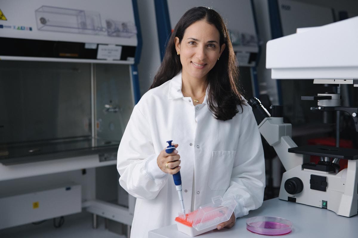 Maayan poses in her lab with a pipette and Petri dish.