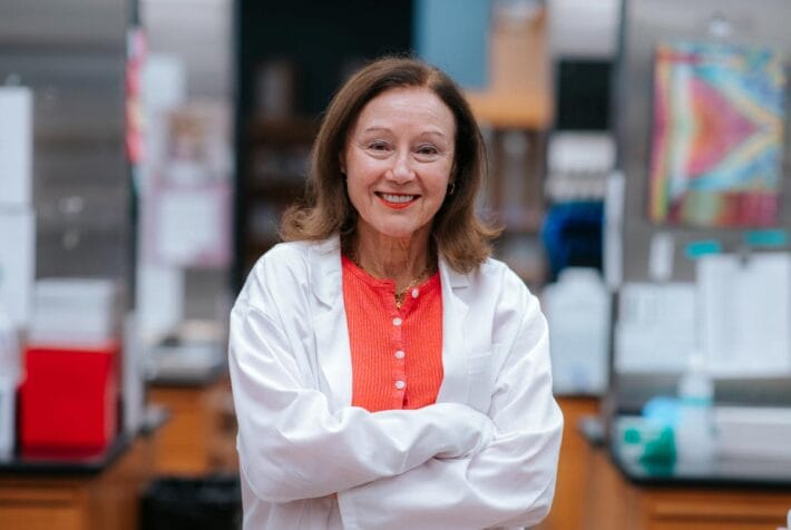 Marianne wearing a white lab coat with her arms crossed.