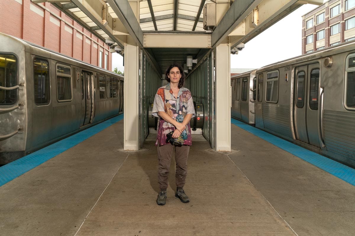 Selva standing at the top of an escalator at the Chicago metro with trains on either side of her. 