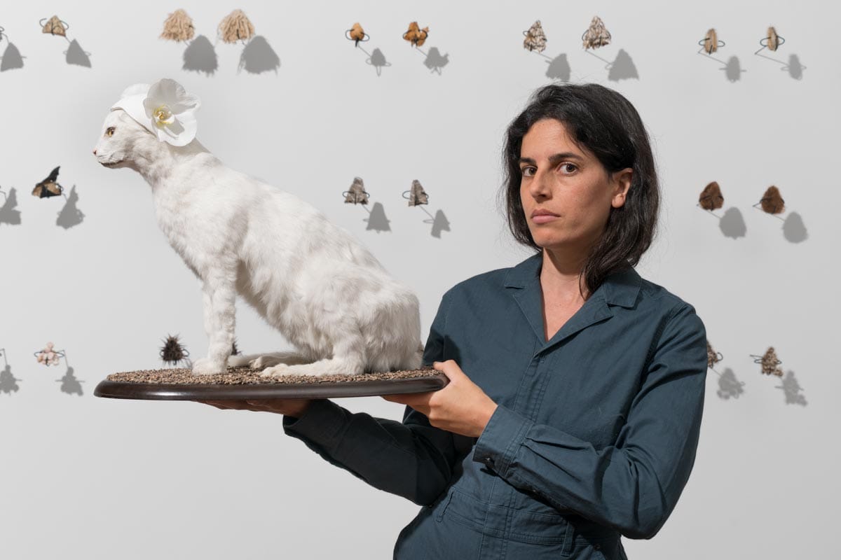 Selva poses holding up a white, taxidermied cat.